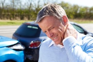 Man injured by car accident, standing outside holding his neck.