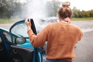 Woman stands outside of car after wreck, holding her neck.