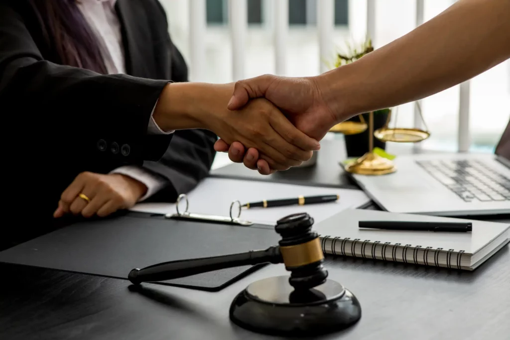 Two people shaking hands near a gavel and legal documents.